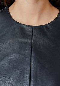 Top en cuir noir avec un col rond et une couture centrale. La texture est lisse avec un léger brillant, mettant en valeur la qualité du matériau.