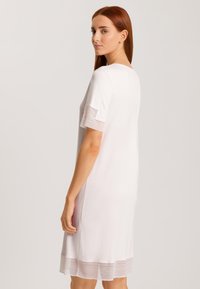 Vestito corto a maniche corte di un delicato rosa chiaro, con scollatura rotonda, dettagli testurizzati sulle maniche e una rifinitura decorativa sul bordo. Tessuto morbido.