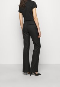 Zwarte slim fit broek met een recht ontwerp, voorzien van een achterzak. Gecombineerd met zwarte hoge hakken en een aansluitend zwart topje.