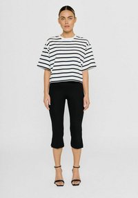 Korte witte blouse met marineblauwe strepen, brede mouwen; gecombineerd met strakke zwarte capri-broeken en zwarte sandalen met bandjes. Eenvoudige casual outfit.