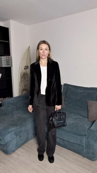 Melns samta žakete pār baltu kreklu, kombinēts ar melnām biksēm. Persona tur mazu melnu rokassomu. Mīksts tekstūra uz zilā dīvāna.