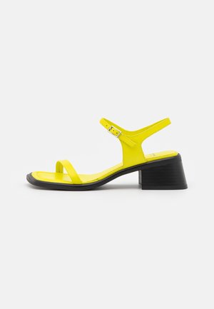 Yellow leather sandal with a sleek design, featuring a block heel, thin straps, and a buckle closure. Smooth texture with a glossy finish.