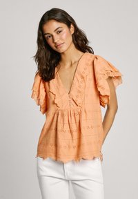 Blusa color pesca con maniche arricciate, scollatura a V, motivi ricamati e vita arricciata. Presenta dettagli con bottoni e orlo scallop.