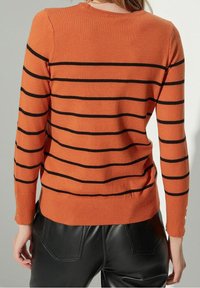 Oranje gebreide trui met zwarte horizontale strepen, geribbelde halslijn en manchetten, met knopen op de mouwen, gecombineerd met zwarte leren broek.