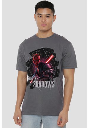 Junger Mann trägt ein graues T-Shirt mit Darth Maul mit rotem Lichtschwert und dem Text „From the Shadows“ auf der Vorderseite.