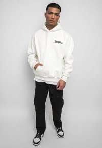 Sweat à capuche blanc avec poche frontale et texte 'Dropsize' en noir. Porté avec un pantalon cargo noir et des baskets noir et blanc. Tissu lisse, coupe décontractée.