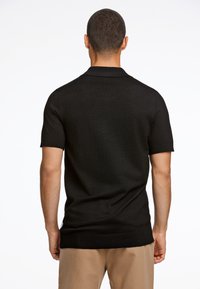 Camisa polo negra de manga corta con un diseño de punto texturizado, silueta ajustada y cuello y dobladillo acanalados. Sin logotipos ni patrones visibles.