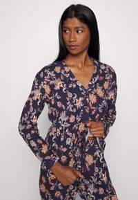 Navyblå blommönstrad pyjamasuppsättning med långa ärmar, prydd med livfulla orange, röda och blå blommor, knappstängning framtill och dragsko i midjan.