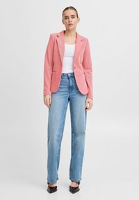 Rosa skräddarsydd kavaj med en enda knapp, kombinerad med ljusblå raka jeans och svarta spetsiga skor. Släta texturer, avslappnad passform.