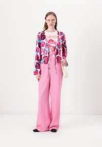Multicolored floral cardigan in pink and blue, layered over a white graphic shirt; paired with high-waisted, pink wide-leg trousers.