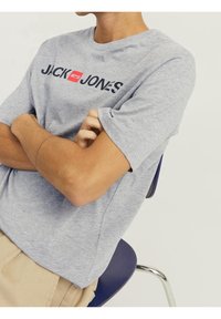 Camiseta de algodón gris con cuello redondo y mangas cortas, que presenta "JACK & JONES" impreso en colores contrastantes y en negrita a lo largo del pecho.