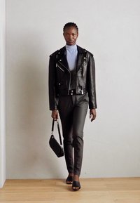 Zwarte leren bikerjack over een lichtblauwe coltrui, gecombineerd met strakke zwarte broek en open te toe zwarte sandalen, met een kleine zwarte tas.