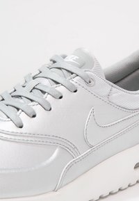 Baskets de sport argentées avec une tige en synthétique lisse, des lacets plats, un col rembourré et un logo Nike discret sur la languette et sur le côté. Semelle blanche.