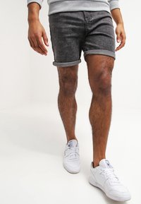 Pantalones cortos de mezclilla gris con puños enrollados, combinados con zapatillas blancas. Tela con textura visible, diseño ajustado y un look casual.