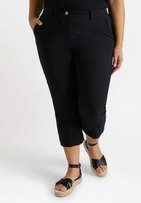 Pantalons noirs cropped avec poches avant, en tissu lisse et léger. Associés à des sandales espadrilles noires à brides.