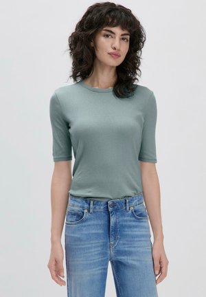 T-shirt vert à manches courtes en tissu doux, avec un col rond. Associé à un jean en denim bleu clair avec poches et coutures contrastées.