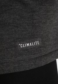 Tessuto grigio con una trama liscia, presenta un logo "CLIMALITE" bianco vicino alla cucitura, evidenziando un design semplice e uno stile atletico.