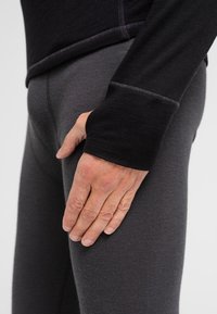 Top negro de manga larga con agujeros para los pulgares, combinado con pantalones ajustados gris oscuro. Ambos hechos de una tela suave y elástica con costuras visibles.