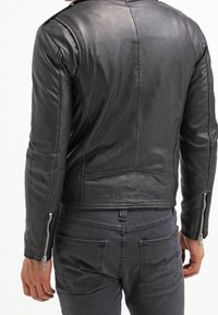 Svart läderjacka med en figurnära design, synliga sömnadsdetaljer och dragkedjeflikar. Slät yta, kort längd och ingen framträdande hårdvara.