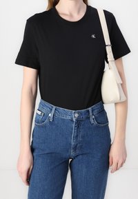 Černé bavlněné tričko s krátkými rukávy a kulatým výstřihem, s malým logem CK na hrudi, spojené s vysokými modrými džínami z denimu.