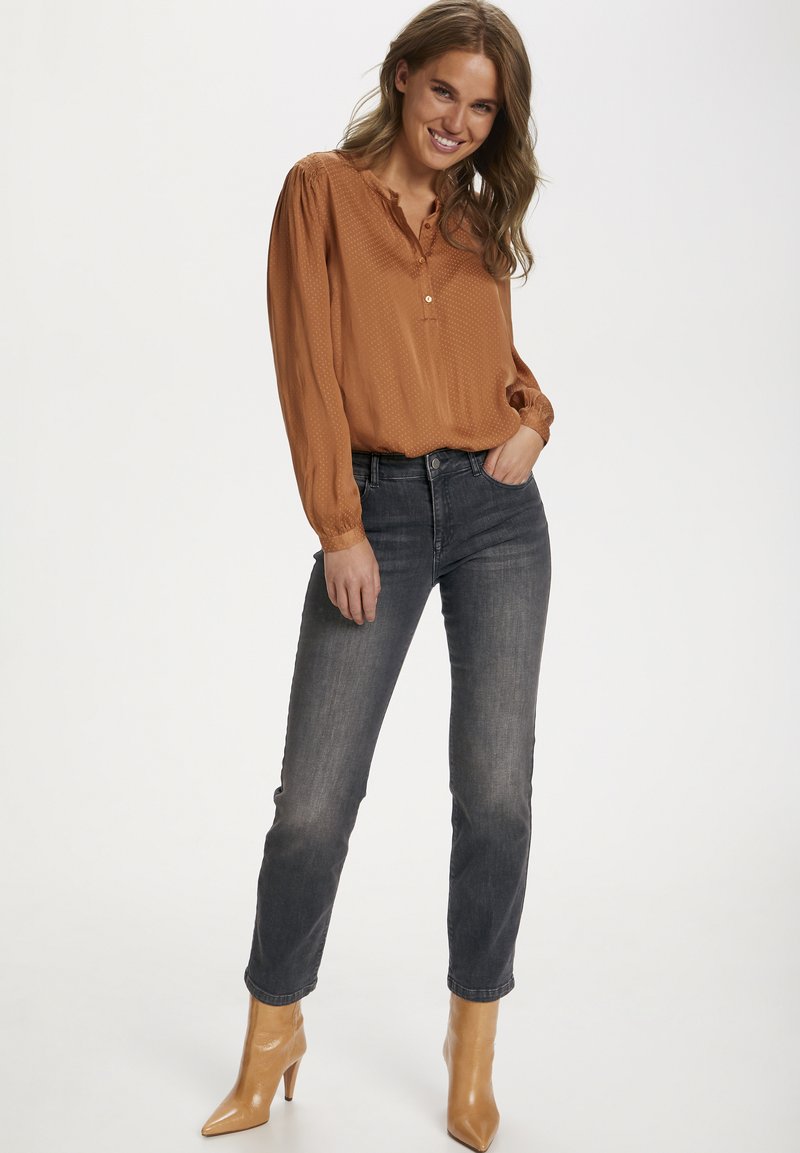 Blusa de manga longa, na cor ferrugem, com decote abotoado e tecido texturizado; combinada com jeans cinza-escuro e sapatos de salto nude com bico fino.