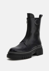Stivali neri alla caviglia con zip laterale, realizzati in materiale liscio, caratterizzati da una suola spessa con scanalature orizzontali e un accento con logo circolare.