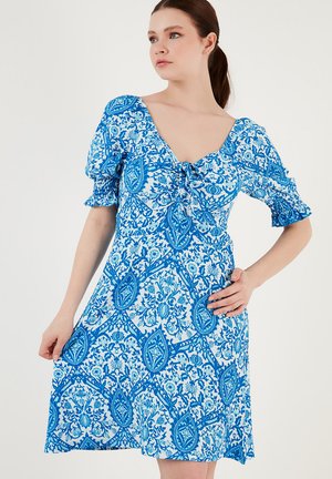 Blue and white patterned dress with puff sleeves, a V-neckline, and a tie front detail. Made of lightweight fabric, knee-length.