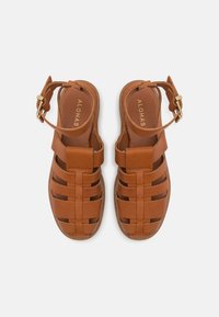 Paire de sandales en cuir marron avec plusieurs brides et boucles à la cheville, nom de la marque ALOHAS visible sur les semelles intérieures, vue de dessus sur fond blanc.