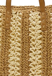 Vævet strå taske med beige og creme skiftende mønstre, der har to brune læderhåndtag med korssting detaljer.