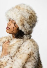 Cappello e cappotto in pelliccia sintetica beige con motivo a macchie marroni. Il cappello ha una consistenza morbida e soffice, mentre il cappotto presenta una sensazione altrettanto lussuosa.
