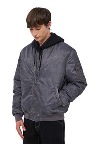 Szara kurtka bombowiec o fakturowanym wykończeniu, z przodu na zamek, z bocznymi kieszeniami i prążkowanymi mankietami. Nałożona na czarną bluzę z kapturem.