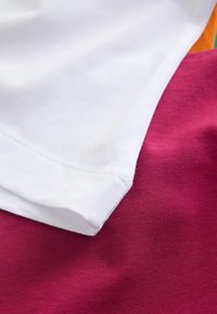 Bavlnené tričká naskladané spolu v bielej, ružovej a oranžovej farbe. Mäkká textúra s viditeľnými detailmi švov a hladkými okrajmi.