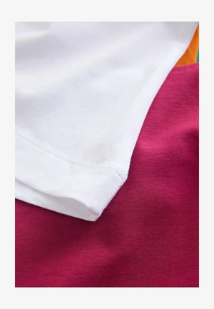 Katoenen T-shirts gestapeld in wit, roze en oranje. Zachte textuur met zichtbare stikdetails en gladde randen.