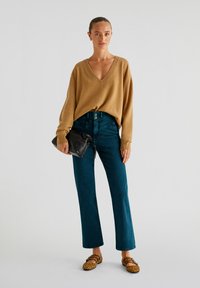 Kamelsininen V-kaula-aukkosetä, korkea vyötärö teal-farkut, musta clutch-laukku ja ruskeat leopardikuosiset ballerinat. Pehmeä rakenne, rento istuvuus, minimaalinen yksityiskohtaisuus.
