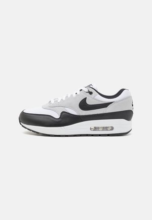 Biało-szaro-czarny but sportowy Nike Air Max z widoczną podeszwą z poduszką powietrzną, czarnym logo Swoosh i białymi sznurówkami na jednolitym tle.