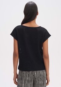 Top nero a maglia con maniche corte, vestibilità ampia e texture a rete aperta. Indossato sopra pantaloni larghi a righe.