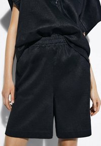 Svarta shorts gjorda av texturerad tyg, med en elastisk midja och sidofickor, med en lös passform.