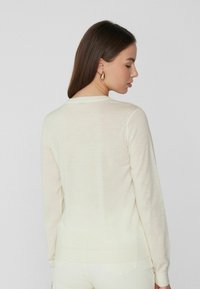 Suéter color crema claro hecho de un material suave y fino de punto, con escote redondo y mangas largas con un corte ligeramente ajustado.