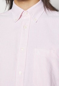 Chemise à rayures roses et blanches avec col, munie d'une poche poitrine unique et d'un détail brodé à l'avant.