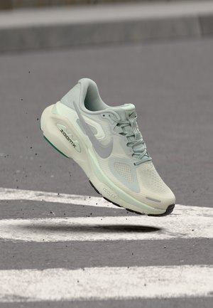 Pantof sport Nike ZoomX React gri deschis plutind deasupra asfaltului cu marcaje albe pe stradă și mici resturi în jur.