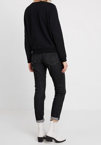 Felpa nera, skinny jeans scuri con orli risvolti e stivaletti bianchi alla caviglia con finitura testurizzata. Vista da dietro.