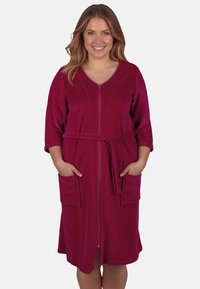 Accappatoio fucsia con zip frontale, maniche a tre quarti, due tasche anteriori e cintura coordinata. Tessuto morbido e liscio.