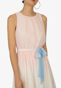 Ærmeløs kjole i pastel pink og hvid gradient med en indsamlet liv og et lyseblåt bælte, der er bundet i en sløjfe i taljen.