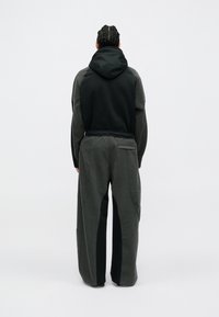Chaqueta con capucha con la parte superior negra y la parte inferior de un gris oscuro texturizado; diseño de pierna ancha, bolsillo canguro en la parte frontal y cinturilla elástica.