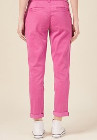 Pink cotton chinos with a relaxed fit, rolled cuffs, and back pockets, paired with white high-top sneakers against a neutral background.