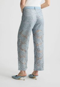 Pantaloni in pizzo azzurro chiaro con motivi floreali; vestibilità rilassata, lucentezza delicata; abbinati a scarpe slip-on azzurro chiaro con accenti di brillantini.