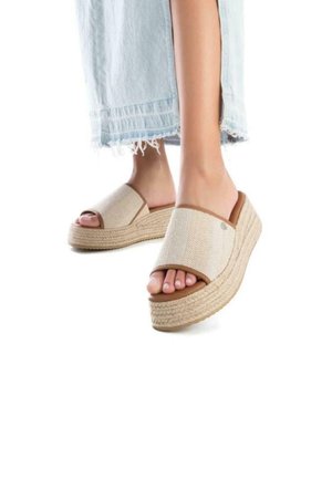 Sandalias de plataforma abiertas en la parte delantera en beige con textura trenzada, acentos marrones y suela estilo cuerda; pie parcialmente visible con falda de mezclilla clara.