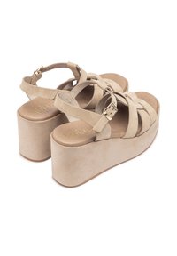 Sandali platform in suede beige con cinturini incrociati, fibbia regolabile e suola spessa. Texture morbida con finitura liscia.
