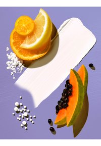 Tranches de citron, orange et papaye avec des graines noires disposées sur un fond violet avec une trace de crème blanche et de petits comprimés blancs.