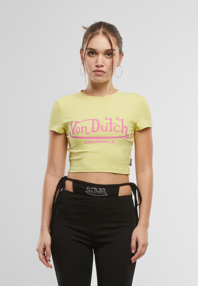 Gul kort t-skjorte med en rosa "Von Dutch Originals" logo. Modellen har på seg svarte bukser med et rhinstein-prydet liv.